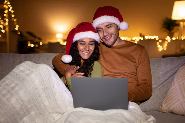 サンタの帽子をかぶったラップトップを介してクリスマス映画を楽しむカップル屋内 — ストック写真