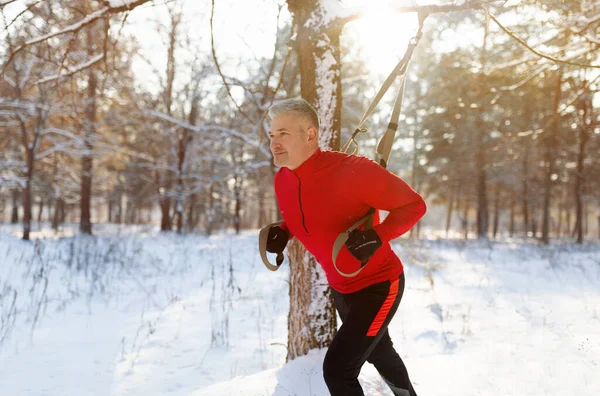 Outdoor endurance exercises. Athletic mature man doing TRX fitness workout at winter park, copy space — Stock Photo, Image