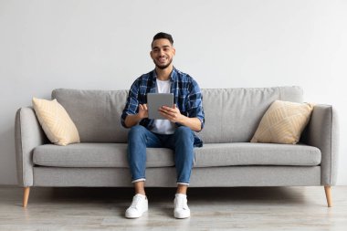 Tablet kullanan gülümseyen bir Arap portresi.