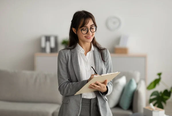 Geconcentreerde succesvolle vrouwelijke psycholoog schrijven in klembord, het aanbieden van professionele counseling diensten — Stockfoto