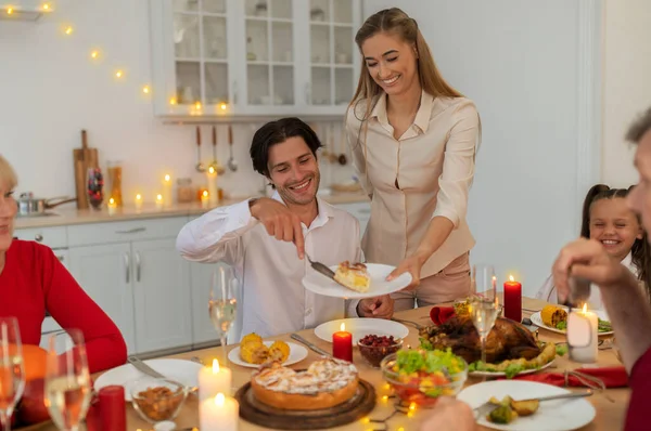 Fiatal nő tesz finom karácsonyi pite a férje tányérjára, ünnepli a karácsonyt a tágabb család otthon — Stock Fotó