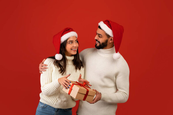 Christmas, new year gifts. Excited arab guy giving Christmas gift to wife, celebrating xmas together, wearing Santa hats — Stock Image Christmas, new year gifts. Excited arab guy giving Christmas gift to wife, celebrating xmas together, wearing Santa hats Royalty Free Stock Images