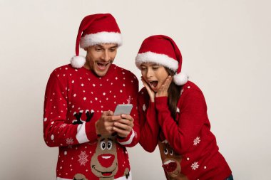 Smartphone ekranına bakan süveter ve Noel Baba Şapkalı Şaşkın çift