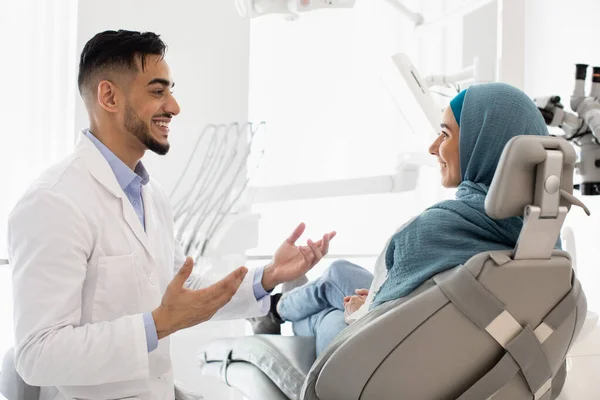 Bonito árabe dentista masculino conversando com muçulmano paciente do sexo feminino na clínica dentária — Fotografia de Stock
