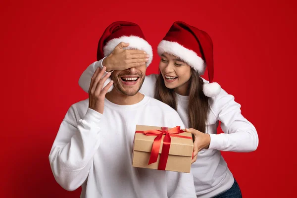 あなたへの贈り物。サンタの帽子の女性はボーイフレンドにクリスマスの驚きを作る — ストック写真