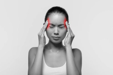 Baş ağrısı çeken Asyalı kadın, şakaklarına dokunuyor.