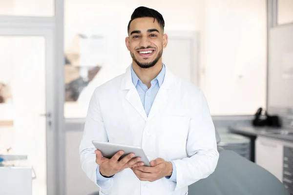 Odontología moderna. Retrato de dentista árabe sonriente con tableta digital en las manos —  Fotos de Stock