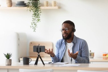 Gözlüklü ve kulaklıklı üzgün genç siyah sakallı öğretmen video dersi veriyor.