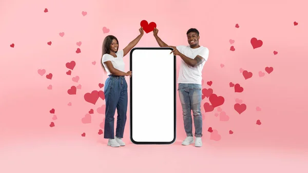 Casal mostrando branco vazio smartphone tela segurando papel coração — Fotografia de Stock