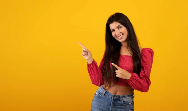 Ευτυχισμένη νεαρή Αρμένισσα κυρία δείχνοντας δύο δάχτυλα στην άκρη του ελεύθερου χώρου διαφημίζοντας το κείμενο ή το σχέδιό σας, κίτρινο φόντο — Φωτογραφία Αρχείου