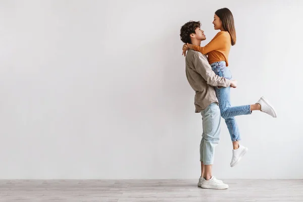 Vista lateral do romântico jovem asiático cara segurando e abraçando sua amada namorada contra a parede do estúdio branco, espaço cópia — Fotografia de Stock