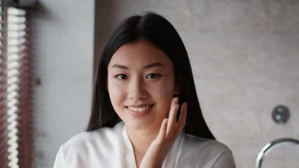 Happy Korean Woman Applying Facial Cream Moisturizing Skin In Bathroom — Stock Video