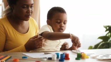 Küçük siyah çocuk ve annesi evde suluboya resim çiziyorlar.