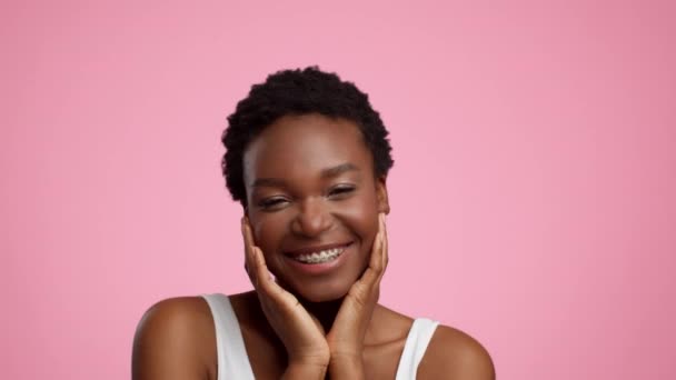 Nero donna con Bretelle sorridente toccare faccia oltre rosa sfondo — Video Stock