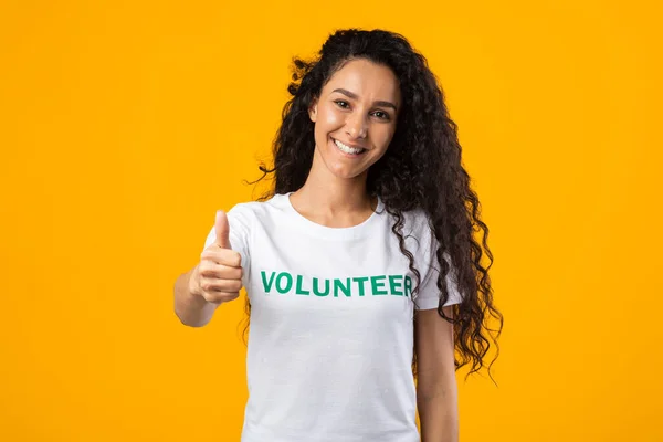 Εθελοντής Γυναίκα Εμφανίζεται Σαν Gesturing Thumbs-Up στέκεται σε κίτρινο φόντο — Φωτογραφία Αρχείου