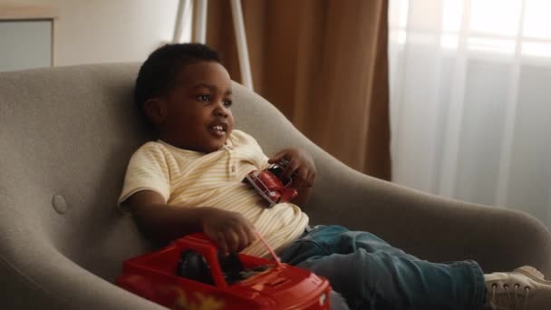 Carino piccolo nero ragazzo giocare con giocattolo auto mentre seduto in sedia — Video Stock