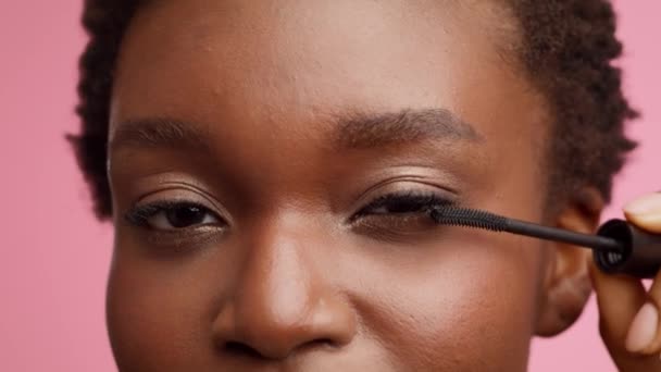 Μαύρη γυναίκα εφαρμογή μάσκαρα στις βλεφαρίδες πάνω από ροζ φόντο, περικοπή — Αρχείο Βίντεο