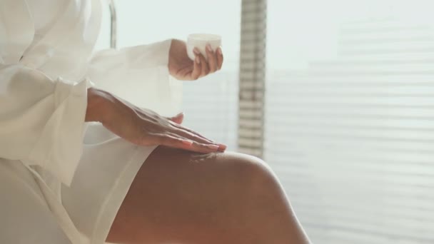 Procédures beauté lifting de la peau. Dame afro-américaine méconnaissable appliquant de la crème corporelle sur la peau de ses jambes, espace libre — Video