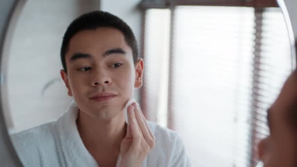 Японский парень наносит лосьон для лица с хлопчатобумажной палочкой в ванной комнате — стоковое видео