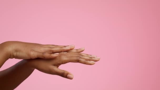 ピンクの背景にモイスチャライザークリームを適用するアフリカの女性の手、クロップ — ストック動画