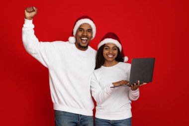 Noel Baba şapkalı duygusal siyahi aşıklar dizüstü bilgisayar tutuyorlar.