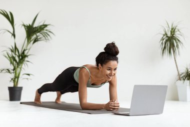 Yurt içi eğitimler. Spor Genç Kadın Dizüstü bilgisayarın önünde Plank Egzersizi Yapıyor