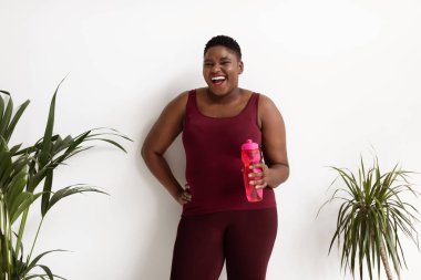Neşeli Afrikalı Amerikalı kadın artı boyut şişesi ve su.