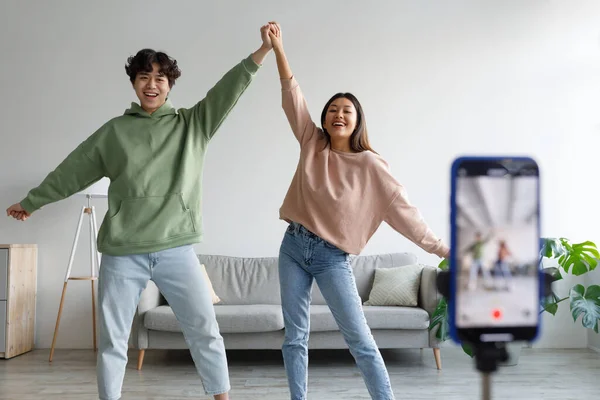 Happy young Asian couple making video on cellphone, dancing in front of camera at home — 图库照片