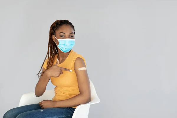 Vacunación contra el Coronavirus. Joven mujer negra con máscara apuntando a la tirita en el brazo, vacunándose contra el covidio —  Fotos de Stock
