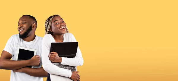 Gadget Addiction. Cheerful Black Man And Woman Embracing Digital Tablet And Laptop