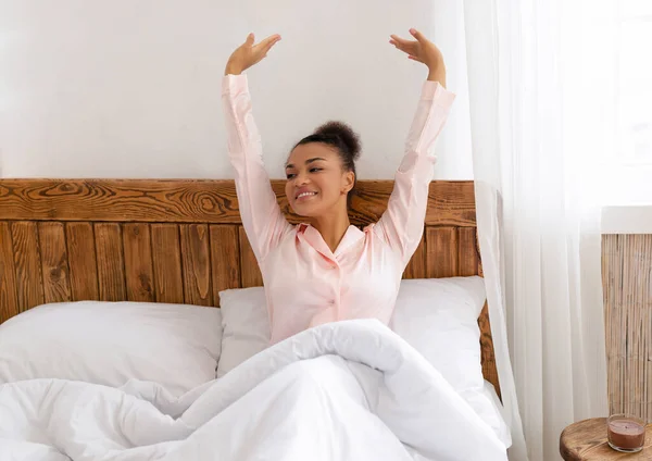 Good morning, world. Well-rested african american woman sitting and stretching in comfy bed, raising hands and smiling — Stock Photo, Image