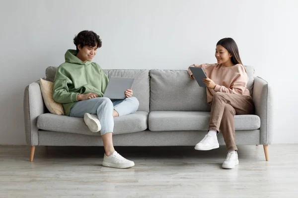 Όμορφος νεαρός Ασιάτης και η φίλη του χρησιμοποιούν σύγχρονα gadgets, ενώ κάθεται στον καναπέ στο σπίτι, αντιγραφή χώρου — Φωτογραφία Αρχείου