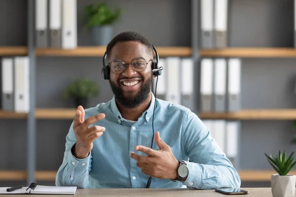 Glimlachende vriendelijke jonge Afrikaans-Amerikaanse bebaarde man met bril en koptelefoon gebaren en kijkt naar camera — Stockfoto