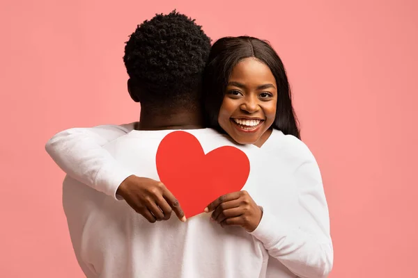 Felice donna afro-americana abbracciare il suo ragazzo, tenendo il cuore rosso — Foto Stock