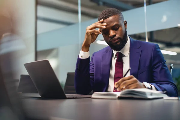 Pensativo hombre negro CEO trabajando en la oficina, tomando notas — Foto de Stock
