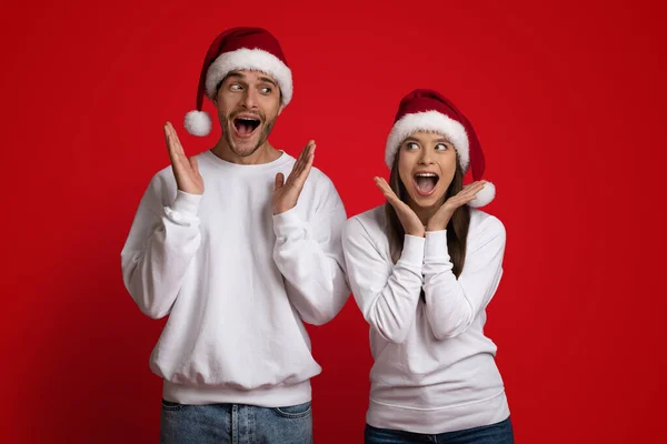 Offre choquante. Couple surpris portant des chapeaux de Père Noël écartant les mains, s'exclamant avec excitation — Photo