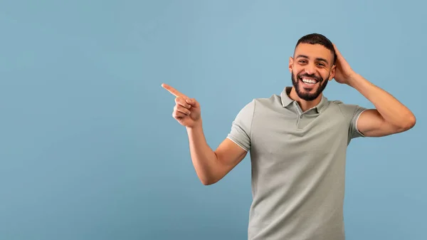 Guarda questa offerta. Uomo arabo eccitato indicando da parte mostrando spazio vuoto per il testo o l'annuncio, sfondo blu — Foto Stock