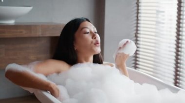 Asyalı kadın banyoda köpükle banyo yaparken eğleniyor.
