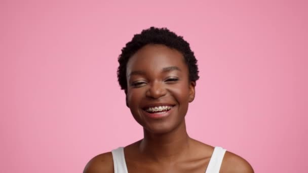 Glückliche Afroamerikanerin posiert lächelnd auf rosa Hintergrund — Stockvideo