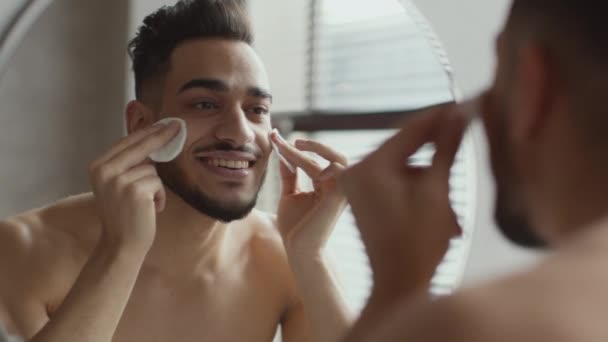 Увеличить портрет молодого красивого ухоженного парня, чистящего лицо увлажняющим лосьоном и двумя хлопчатобумажными прокладками — стоковое видео