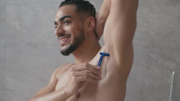 Hygienische Verfahren. Junger nackter glücklicher Mann aus dem Mittleren Osten rasiert sich die Achselhöhlen, während er zu Hause morgens duscht — Stockvideo