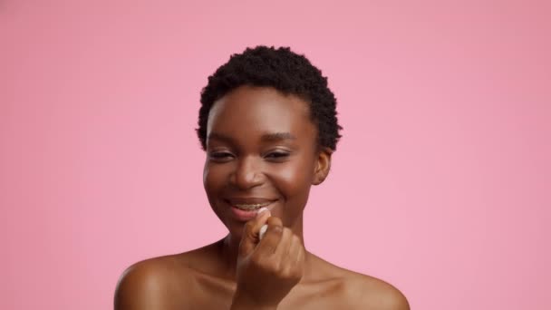 Afroamerikanerin trägt Lippenbalsam über rosa Hintergrund auf — Stockvideo