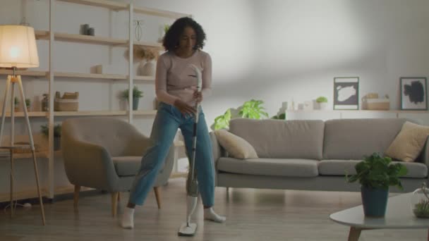 Hausreinigung macht Spaß. Junge positive Afroamerikanerin wäscht Fußbodenameise zu Hause und singt in Wischmopp wie Mikrofon — Stockvideo