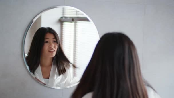 Жінка - азіатка, яка торкається волосся, маючи розріджене волосся, завершує проблему в ванній кімнаті — стокове відео