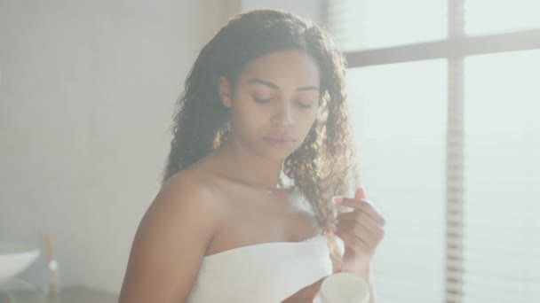 Giovane donna afroamericana pacifica che applica crema per il corpo coccole sulla pelle delle spalle, idratante corpo dopo la doccia — Video Stock