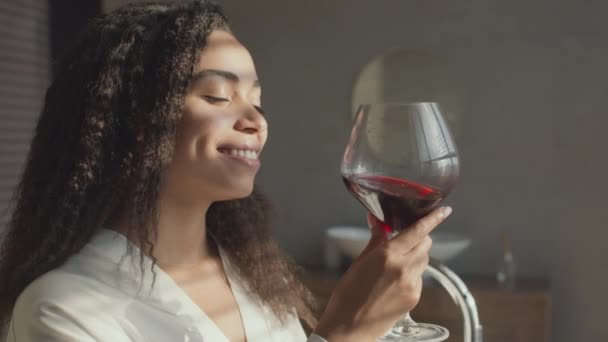 Gros plan portrait de jeune femme afro-américaine insouciante dégustant un verre de vin rouge et profitant du coucher de soleil à la salle de bain — Video