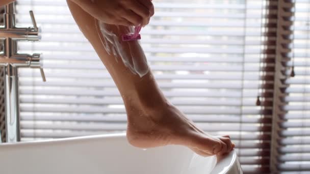 Концепция депиляции. Неузнаваемая женщина бреет ноги с бритвой и пеной в ванной — стоковое видео