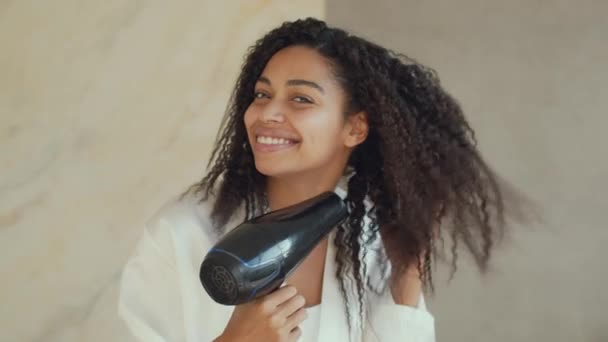 Specchio punto di vista ritratto di giovane donna afro-americana felice asciugandosi i capelli ricci con asciugacapelli in bagno, zoom in — Video Stock