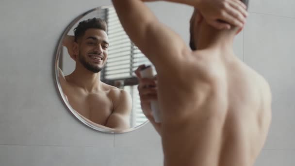 Everyday hygiene concept. Over shoulder portrait of young handsome shirtless arab guy spraying deodorant on his armpit — Stockvideo