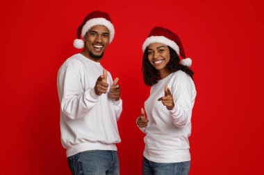 Noel Baba şapkalı neşeli siyah aşıklar kamerayı işaret ediyor.